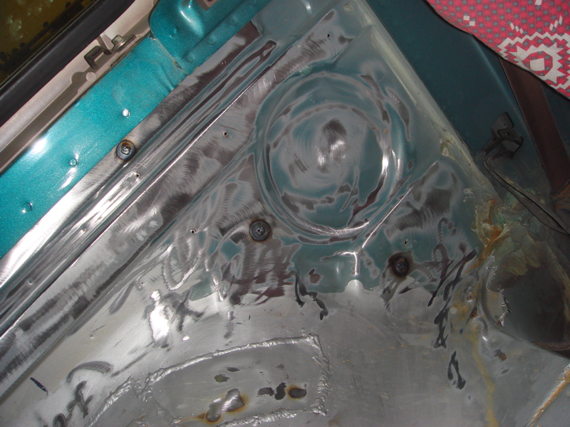 Close-up of bare metal and teal painted interior fender area with visible welds and screw heads