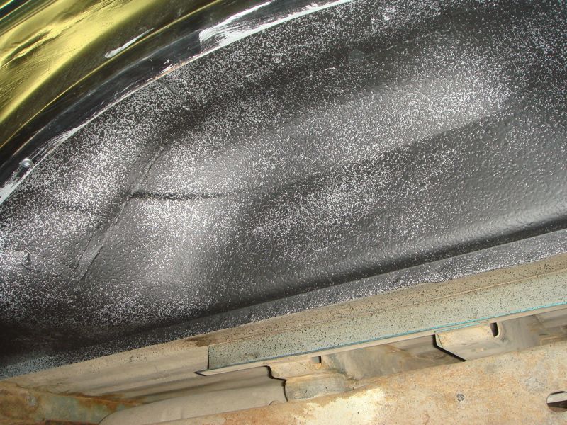 Inner fender well with black spray-on bedliner material and some white overspray. Chassis components visible below