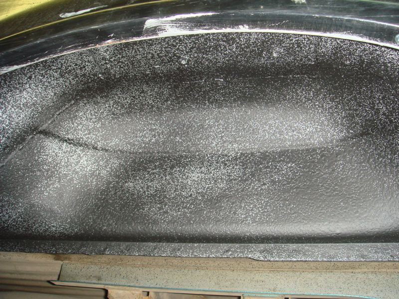 Close-up of a vehicle's inner fender well, coated in black spray-on liner with white flecks