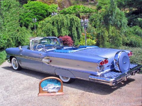 1972 Ford Ranchero - A vintage blue convertible with a continental kit is parked on a paved surface with lush greenery in the background.