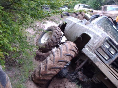 1990 Ford F-150 - A truck is stuck in the mud with its tires partially submerged in the dirt, while other vehicles are visible in the background.