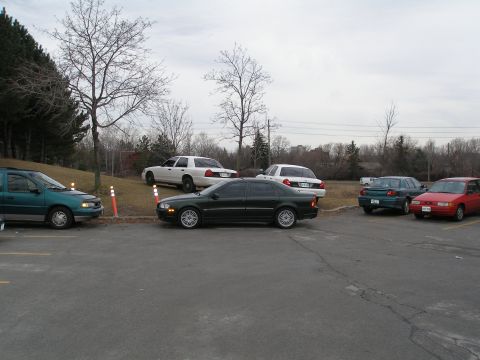 2003 Ford Crown Victoria - Several cars are parked in an outdoor lot under an overcast sky.