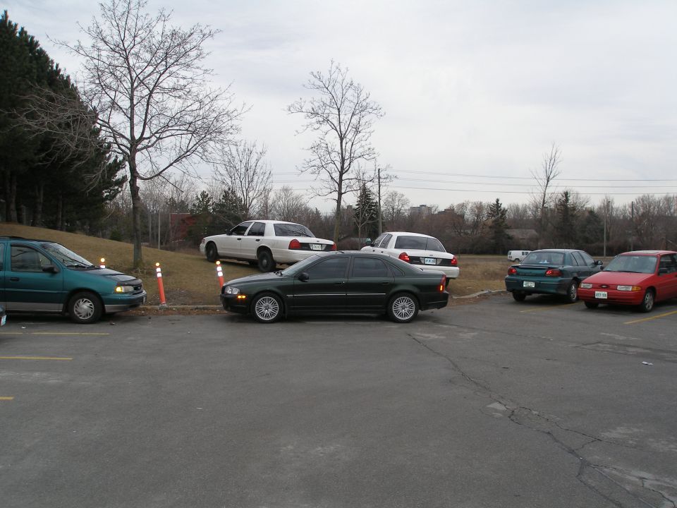Dark sedan parked in a lot, side view. Other vehicles visible