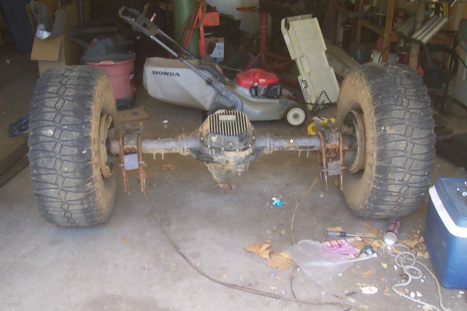 Solid rear axle with mud tires removed from vehicle on garage floor