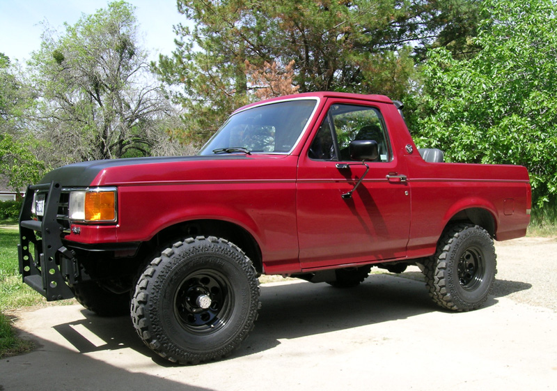 1991 Ford Bronco, red, with black aftermarket front bumper and off-road tires