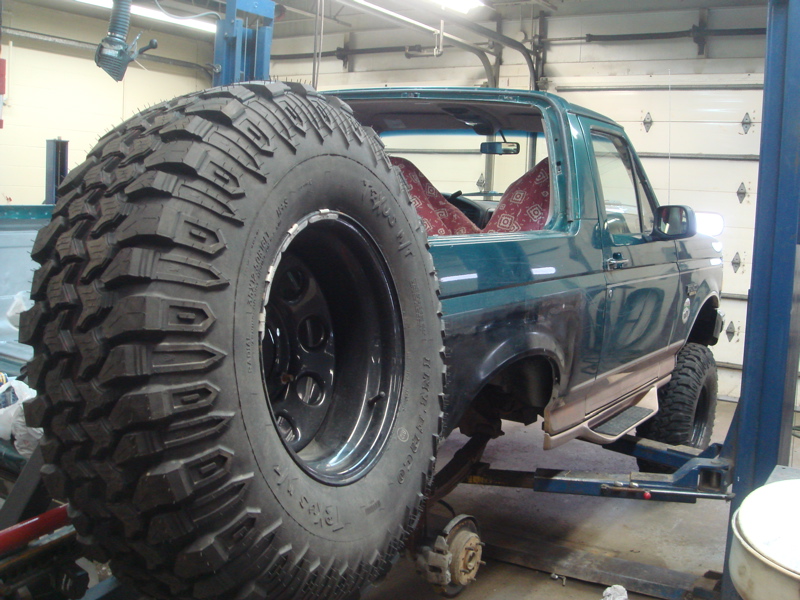 Green Ford Bronco on lift, spare tire mounted on rear, missing rear bumper and tailgate