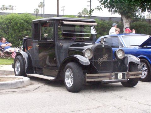 1990 Ford Bronco - A classic black Dodge car with a Route 66 license plate is displayed at a car show, with other vehicles visible in the background.