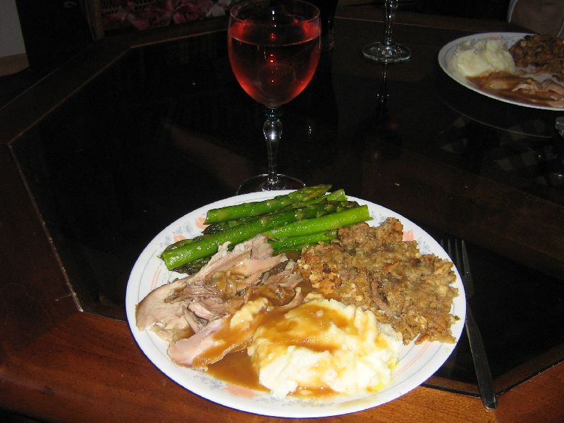 Plate of food with turkey, mashed potatoes, asparagus, and stuffing, next to a glass of red wine