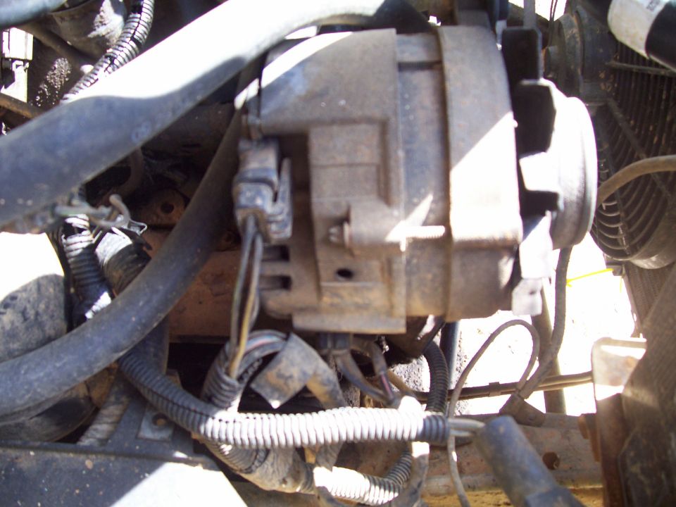 Close-up of an alternator with wiring harness and hoses in an engine bay