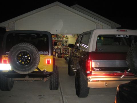 2001 Jeep Wrangler - Two SUVs are parked in front of a garage, one yellow Jeep Wrangler and one red Ford Bronco.