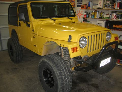 2001 Jeep Wrangler - A yellow 2001 Jeep Wrangler is parked indoors, showing its front three-quarter view with a black soft top and aftermarket bumper.