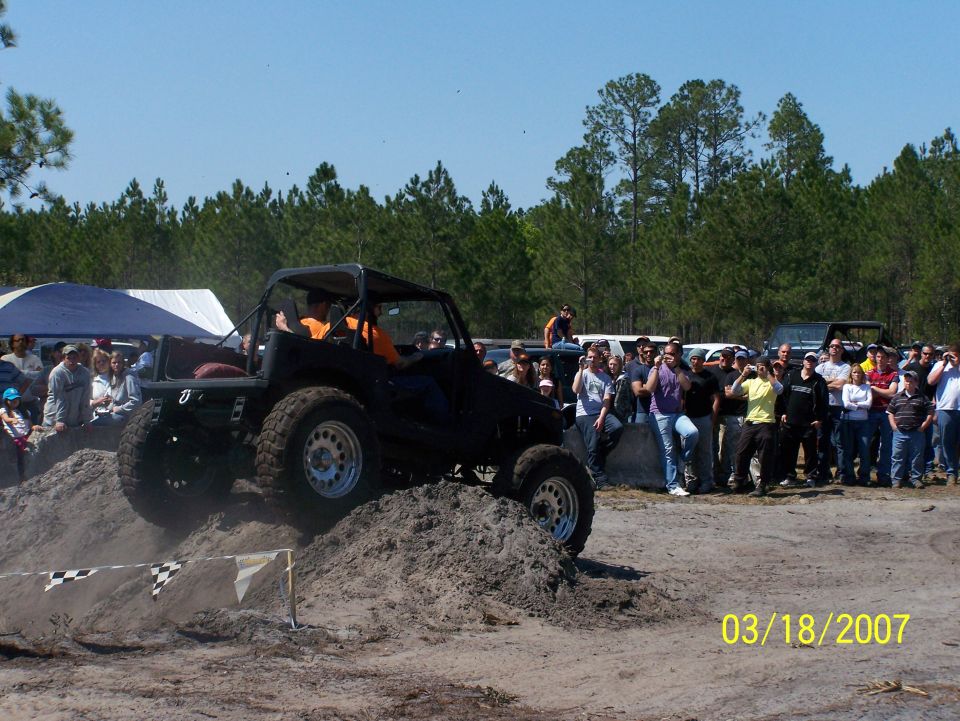 Off-road vehicle with a roll cage climbing a dirt hill in front of a crowd. Date stamp shows 03/18/2007