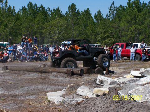1989 Ford Bronco - An off-road vehicle navigates an obstacle course with spectators gathered around.