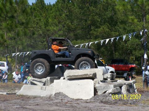 1989 Ford Bronco - An off-road SUV navigates a challenging obstacle course, with spectators watching in the background.