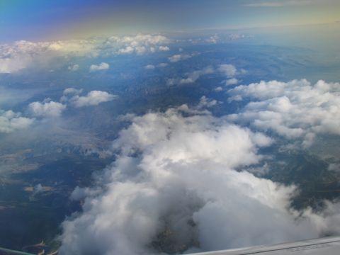 1995 Ford C-350 (Centurion Conversions) - View from an airplane window shows clouds and a distant rainbow over a mountainous landscape.