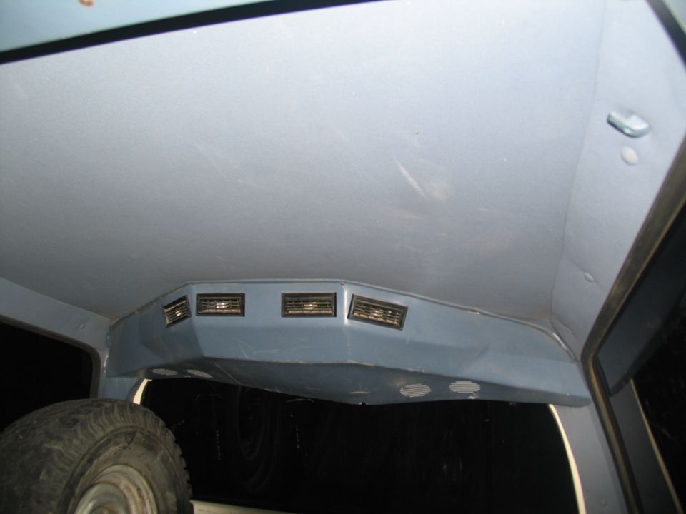 Interior shot of a vehicle's headliner with a custom console housing air vents and a spare tire visible