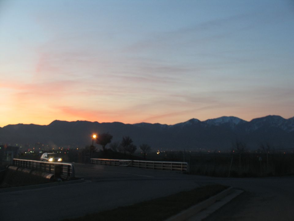 Sunset over mountains with a pickup truck on a road and city lights