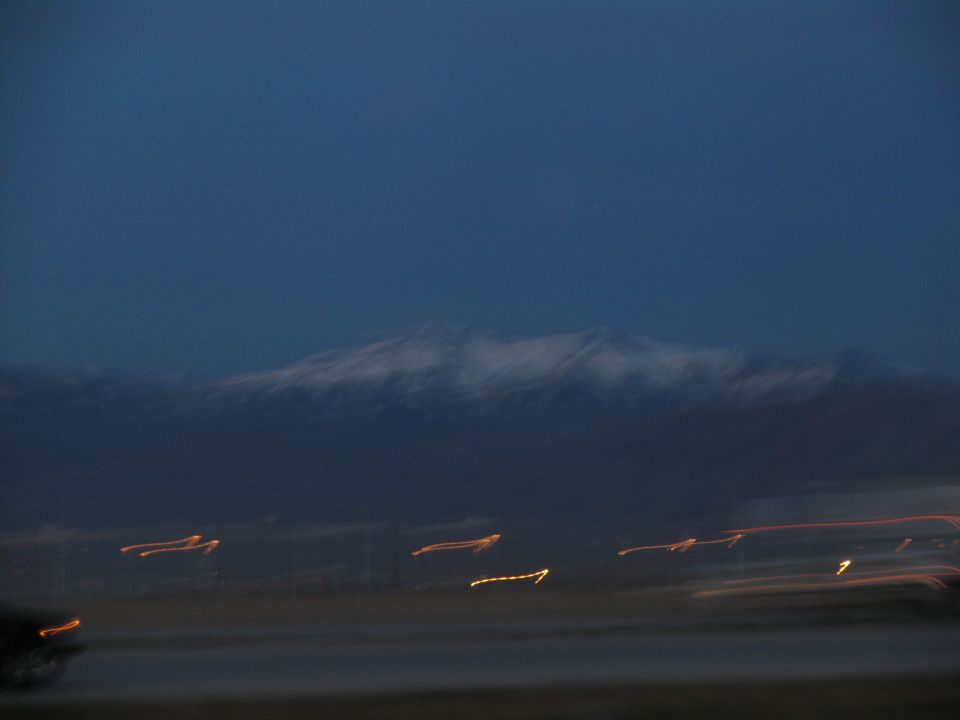 Blurry mountain range at dusk with streaks of orange and yellow lights in the foreground