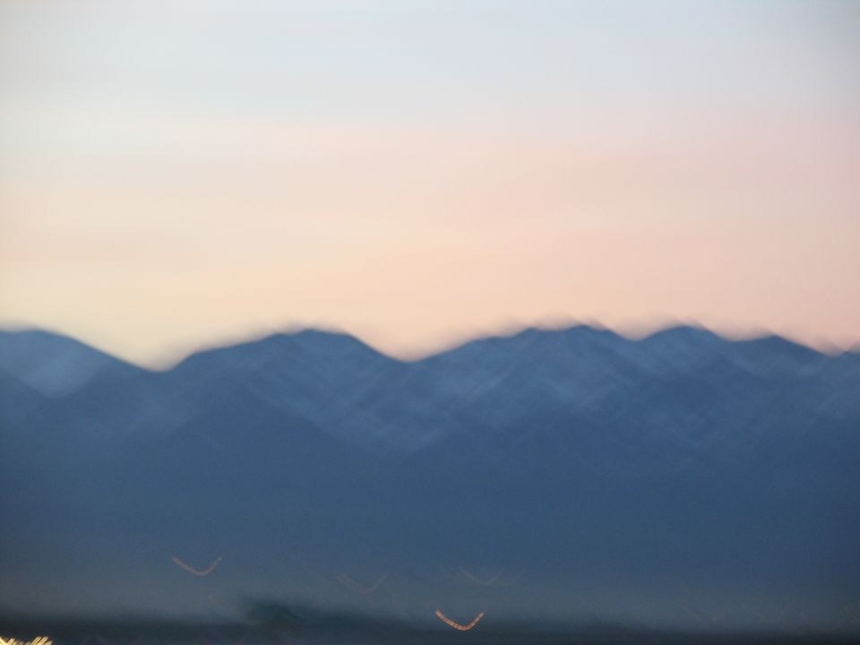 Blurry mountain range against a pink and white sky at dusk