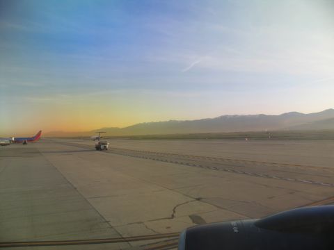 1995 Ford C-350 (Centurion Conversions) - View of an airport tarmac during sunrise, with mountains on the horizon and airplanes visible.