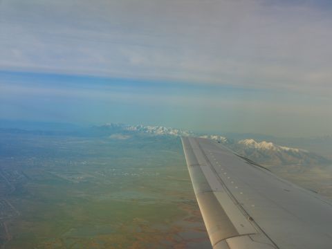 1995 Ford C-350 (Centurion Conversions) - View from an airplane window shows a wing and a distant mountain range under a hazy sky.