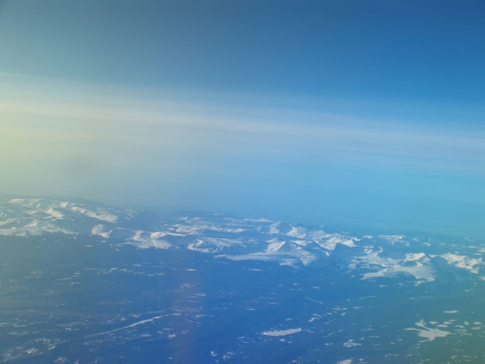 View of snow-covered mountains and forested land from an airplane