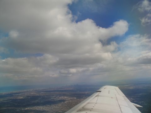 1995 Ford C-350 (Centurion Conversions) - Looking down from an airplane at a city skyline below a cloudy sky.