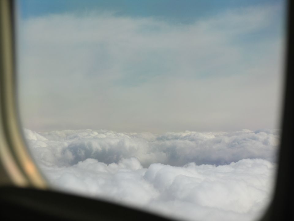 View from an airplane window looking out at a vast expanse of white clouds under a pale blue sky