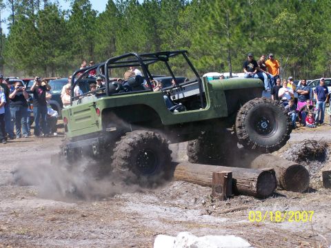 1989 Ford Bronco - Spectators watch as a modified off-road vehicle navigates a log obstacle course.