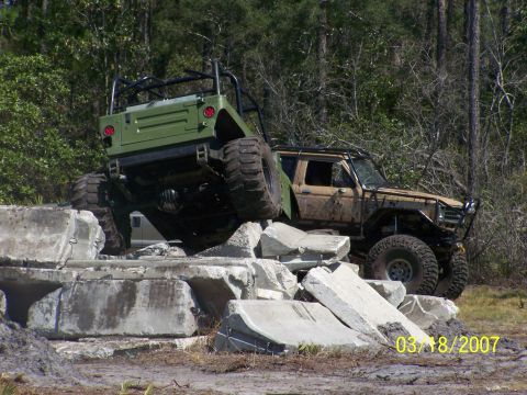 1989 Ford Bronco - Two off-road vehicles tackle a challenging obstacle course made of concrete barriers.