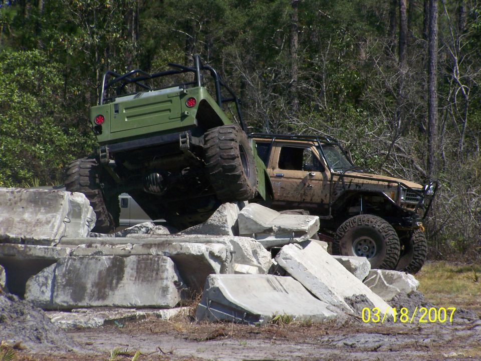 tan 1980s Ford Bronco and green Jeep Wrangler climbing over concrete blocks