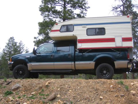 1999 Ford F-250 - A 1999 Ford F-250 Super Duty truck is shown equipped with a camper shell, parked on a dirt road.