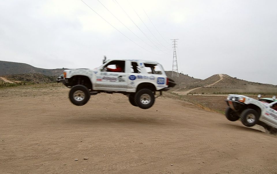 Two off-road trucks airborne over a dirt track, one in mid-jump, the other descending