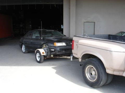 1989 Ford Taurus - A black sedan is being towed by a pickup truck inside a garage.