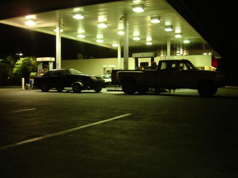 1989 Ford Taurus - Two vehicles are parked at a gas station at night under the illuminated canopy.