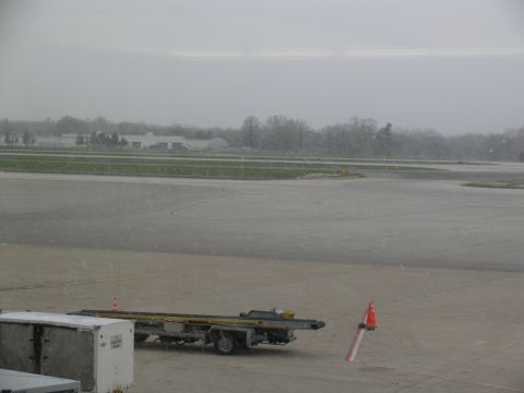 1995 Ford C-350 (Centurion Conversions) - Cargo containers and a tow tractor sit on an airport tarmac during overcast weather.