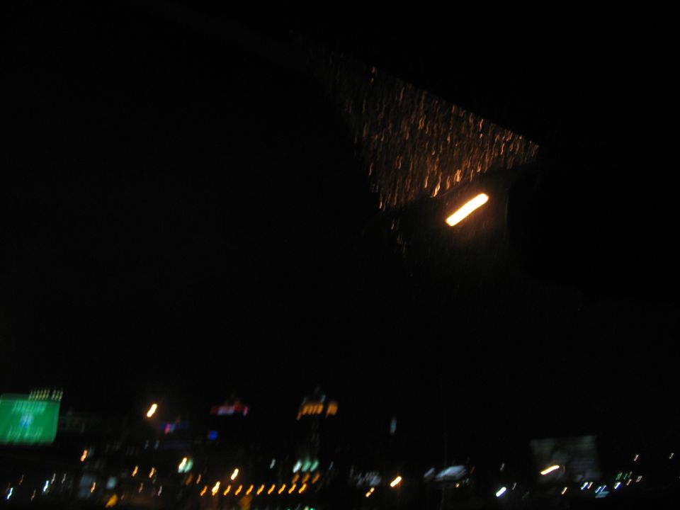 view through a wet windshield at night with blurry lights and buildings in the distance