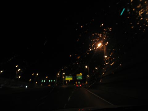1995 Ford C-350 (Centurion Conversions) - Driving on a highway at night through a wet windshield, with streetlights and signs blurred by rain.