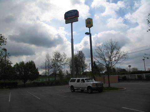 1995 Ford C-350 (Centurion Conversions) - A white SUV is parked in a lot near two hotel signs, under a cloudy sky.