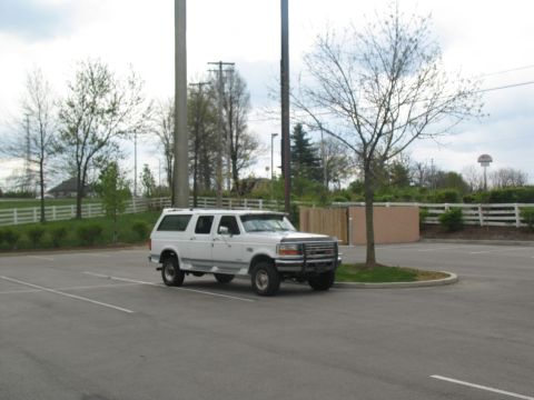 1995 Ford C-350 (Centurion Conversions) - White 1995 Ford C-350 (Centurion Conversions) SUV parked in a lot with trees and fencing in the background.