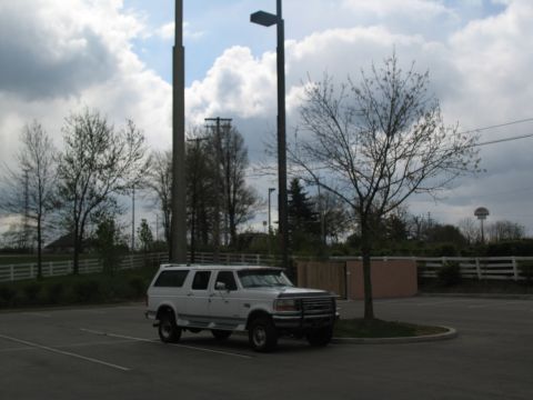 1995 Ford C-350 (Centurion Conversions) - A white SUV is parked in an empty lot under a cloudy sky.