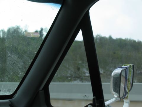 1995 Ford C-350 (Centurion Conversions) - View from inside a vehicle, looking out the side window and mirror at a wooded hillside.