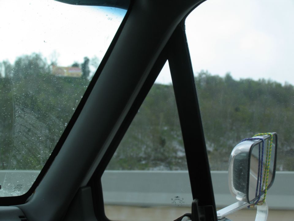 Interior view from driver's side, showing a pillar, side mirror, and a blurry landscape outside