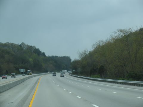 1995 Ford C-350 (Centurion Conversions) - A view from a vehicle traveling on a highway with trees and hills on the side.