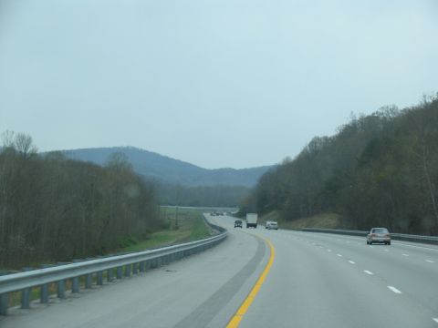 1995 Ford C-350 (Centurion Conversions) - Driving on a highway with a guardrail and trees lining the road.