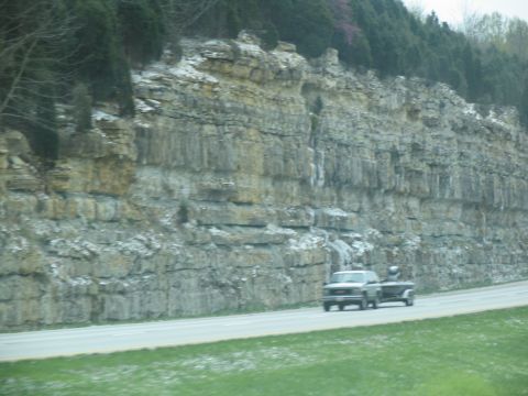 1995 Ford C-350 (Centurion Conversions) - A pickup truck travels down a highway beside a large, layered rock formation.