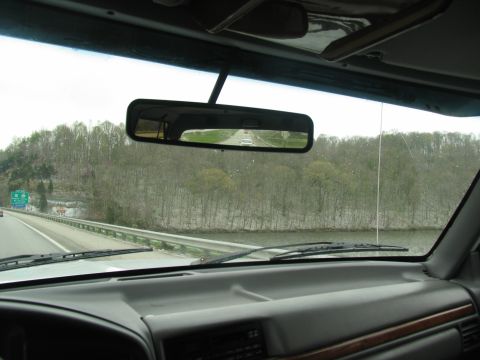 1995 Ford C-350 (Centurion Conversions) - View from inside a vehicle traveling on a highway, with trees and a body of water visible alongside the road.
