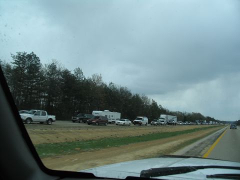 1995 Ford C-350 (Centurion Conversions) - A long line of vehicles are stopped on the highway under a cloudy sky.