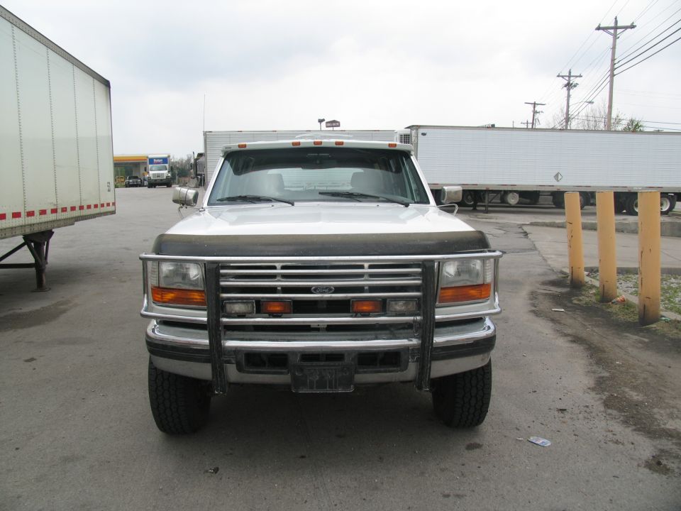 Front view of a white Ford F-Series truck with a chrome grille guard and aftermarket lights