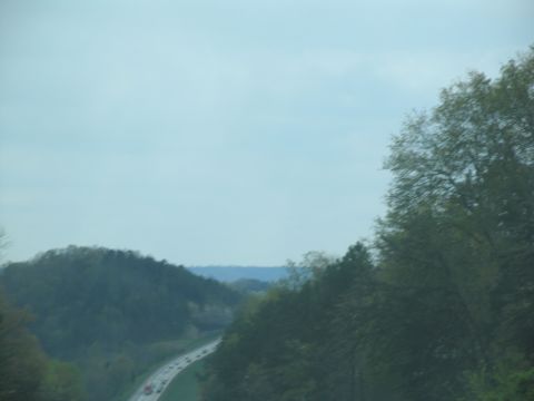 1995 Ford C-350 (Centurion Conversions) - A scenic view of a highway cutting through rolling hills and dense trees under a cloudy sky.